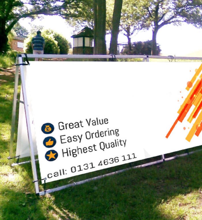 Outdoor portable banner frame displaying a white banner with contact information and promotional messages in a grassy field.