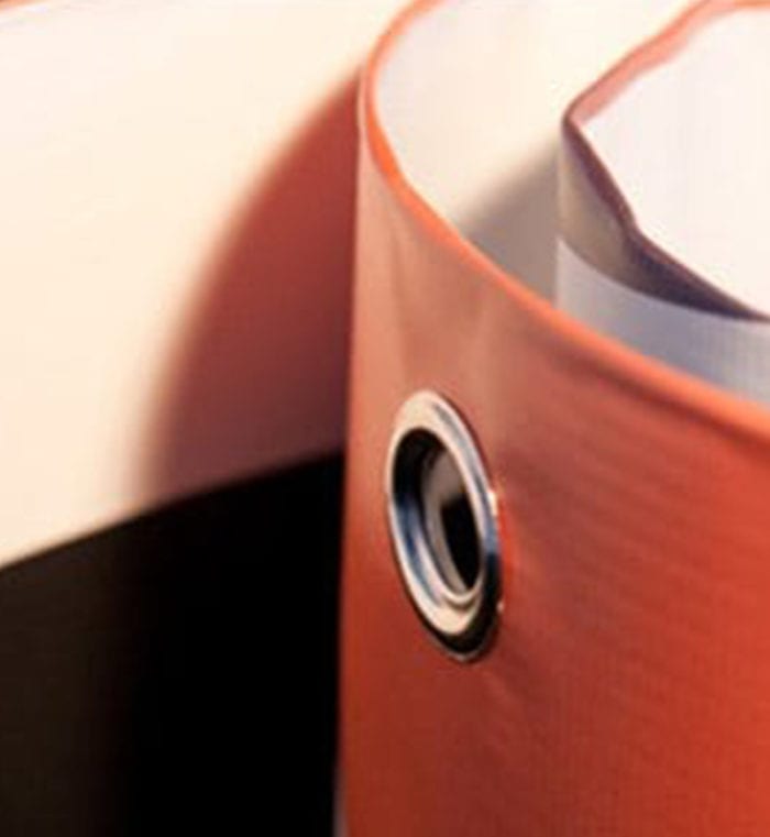 Close-up of an eyelet on a rolled orange PVC banner, signifying readiness for display.