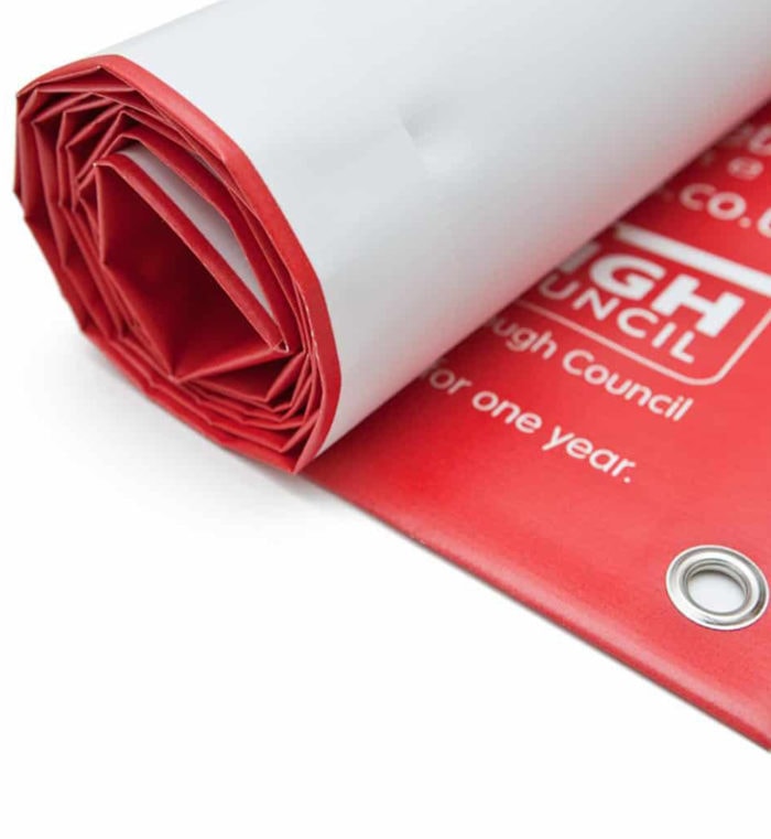 Rolled up red PVC banner with eyelets, ready for outdoor display.
